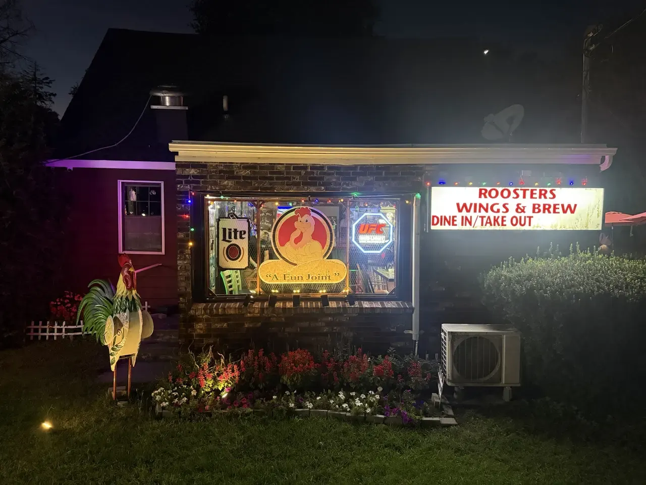 Rooster's Wings & Brew storefront at night, with its illuminated sign and front window.