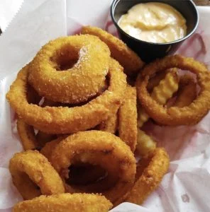 Golden onion rings and crinkle-cut fries with dipping sauce at Rooster's Wings & Brew.