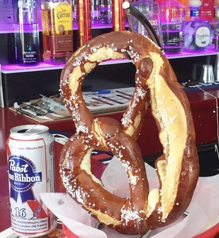 Giant salted soft pretzel with a beer can on the left at Rooster's Wings & Brew