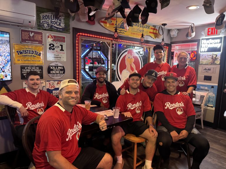 Group wearing red Roosters jerseys gathered inside Roosters Wings & Brew