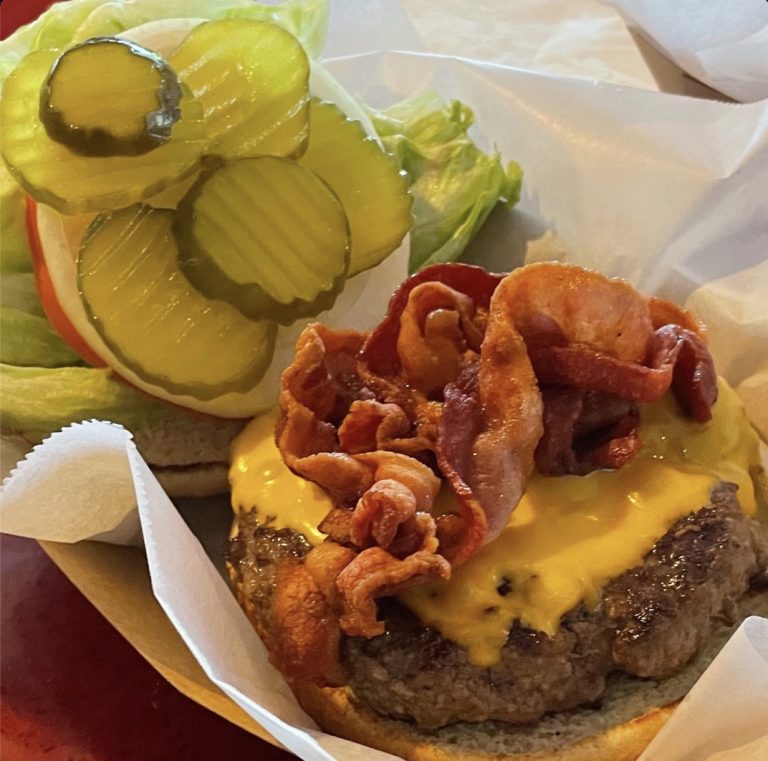 A handmade Rooster's bacon cheeseburger with lettuce, tomato, onion and pickles.